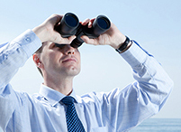 Business man looking through binoculars against blue sky